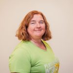 Frau in grünem T-Shirt, Fitness-Ernährungsberaterin, lächelt.