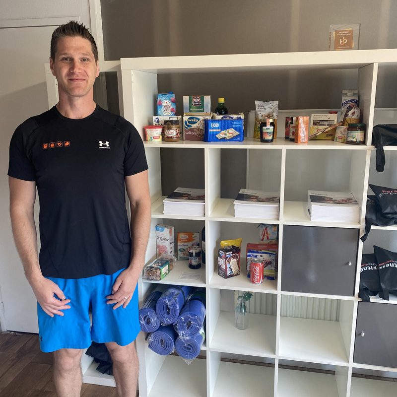 Mann vor Regal mit Fitness-Lebensmitteln und Yogamatten.