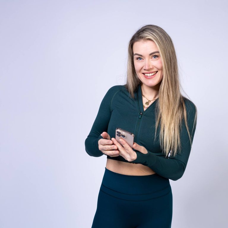 Lachende Frau in Fitnesskleidung mit Smartphone. Dein Partner für effektives Training & gesunde Ernährung per App.